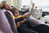 Happy mother and son reading book on living room sofa