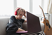 Boy with headphones and laptop on living room sofa