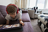 Boy with headphones and digital tablet homeschooling on sofa