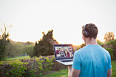 Man with headphones video chatting with friends in garden