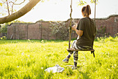 Woman with coffee on swing in sunny garden