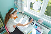 Girl with tablet homeschooling at desk in sunny bedroom