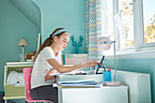 Focused girl homeschooling at desk in bedroom