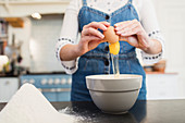 Teenage girl breaking egg into bowl for baking in kitchen