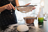 Woman sifting flour of bread dough on kitchen counter
