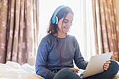 Teenage girl with headphones video chatting on bed