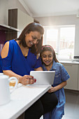 Mother and daughter using digital tablet in kitchen