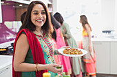 Portrait happy Indian woman in sari eating in kitchen