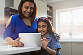 Happy mother and daughter using digital tablet in kitchen