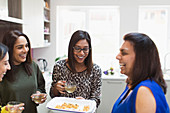 Happy Indian women with tea and food in kitchen
