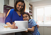 Smiling mother and daughter using digital tablet in kitchen