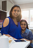 Smiling mother and daughter with digital tablet in kitchen
