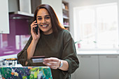 Happy woman with smart phone and credit card at laptop
