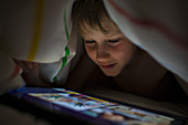 Close up boy using digital tablet under blanket