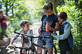 Mother and sons drinking water on bike ride in sunny park