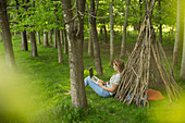 Woman with laptop relaxing at branch teepee in woods