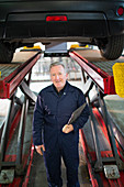 Portrait confident male mechanic under car