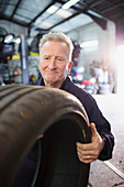 Male mechanic holding tire in auto repair shop
