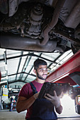 Male mechanic using diagnostic equipment under car