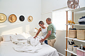 Happy couple making bed in sunny bedroom