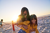 Mother and daughter hugging on sunny sunset beach