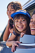 Happy sisters and brother leaning out car window