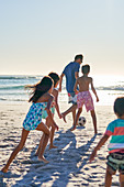 Family playing soccer on sunny ocean beach