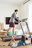 Daughter using laptop next to father on treadmill