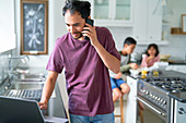 Man working at laptop in kitchen with kids