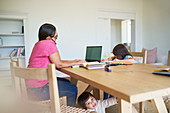 Mother working at laptop with kids playing