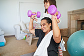Daughter helping mother exercise with dumbbells
