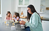 Mother working at laptop, daughters eat breakfast