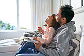 Father feeding popcorn to daughter on sofa