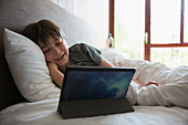 Smiling boy using digital tablet in bed