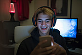 Smiling teenage boy using smart phone in dark room