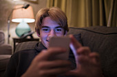 Boy using smart phone on living room sofa