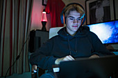 Boy with headset using laptop in dark bedroom