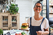 Woman holding cheeseburger on cutting board