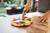 Woman cutting fresh homemade pizza with slicer