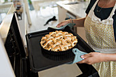 Woman removing fresh baked lattice apple pie