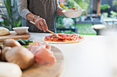 Woman spreading tomato sauce on pizza dough