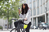 Woman on bicycle using smart phone on city street