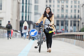 Smiling woman walking bicycle on urban bridge