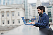 Businessman using laptop on city bridge