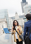 Business people with laptop talking on city bridge