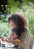 Mother and toddler daughter eating at summer patio