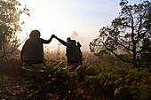 Silhouette couple holding hands hiking at dawn