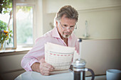 Senior man reading newspaper at laptop