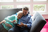 Senior couple cuddling and using tablet on sofa