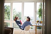 Senior man reading book with feet up at window